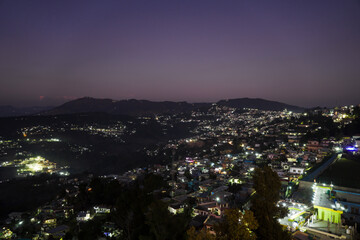 A breathtaking night view of Almora city in Uttarakhand,India.Hills dotted with glowing lights, scattered houses, serene purple sky and faint mountain silhouettes create a peaceful, picturesque scene.
