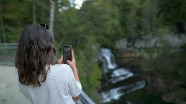 woman takes photo of stunning waterfall surrounded by lush greenery, standing on a viewing platform at Cummins Falls State Park, USA. stunning waterfall Cummins Falls State Park, USA Tennessee