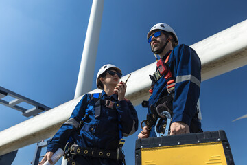Inspection engineers a rotor blade of a wind turbine. Professional Man Maintenance engineers working in wind turbine farm. Engineer Man standing among Wind Energy Turbine.