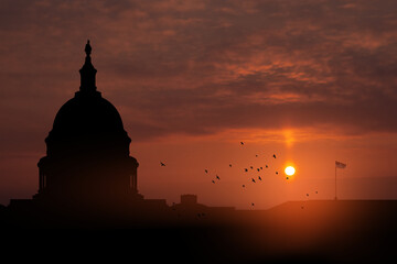 The United States Capitol building silhouette on background of sky at sunset with flying birds in Washington DC, USA