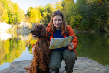Happy 30s woman hiker hiking in mountain lake. Female with a irish setter dog looking at map and...