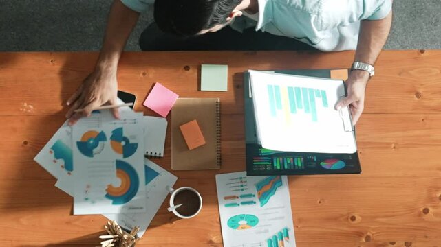 Top aerial view of manager working on laptop while looking at data analysis. Leader compare financial statistic graph while making decision at meeting table with document scatter around. Convocation.
