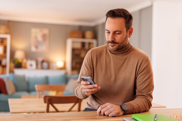 Obraz premium Portrait of serious male entrepreneur reading e-mails over mobile phone while working in home office