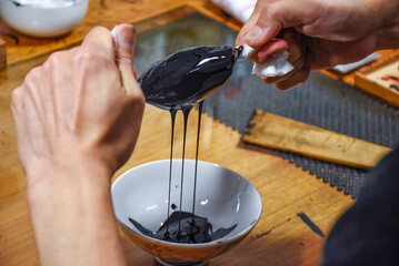 Hands filter the black Japanese raw lacquer, Urushi, through a fine cloth, squeezing out impurities. The process emphasises precision and tradition, and brings out the lustrous purity of the lacquer.