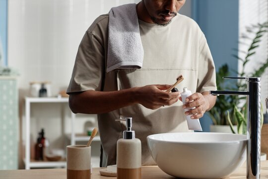 Cropped shot of Black man opening toothpaste tube holding bamboo toothbrush during morning routine in bathroom with zero waste self care products - Powered by Adobe