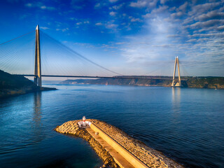 Obraz premium YAVUZ SULTAN SELIM BRIDGE BEYKOZ Stunning Cable-Stayed Bridge Over Azure Waters with Coastal Structures. A breathtaking aerial view of a modern cable-stayed bridge spanning a serene body of water.