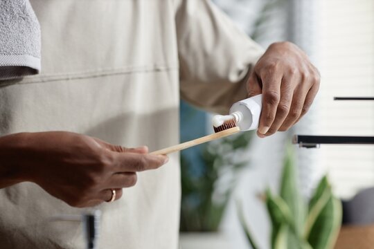 Cropped shot of African American man applying toothpaste on bamboo toothbrush taking care of mouth cavity during morning routine in bathroom using zero waste products, copy space