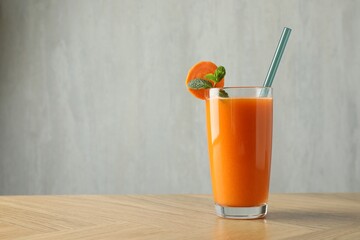 Fresh carrot juice in glass on wooden table against gray background, space for text