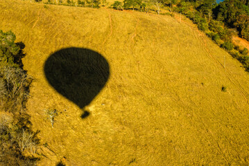 A perfectly defined shadow from a hot air balloon is cast over a golden field, creating a visual composition that combines movement and tranquility. The texture of the dry vegetation, illuminated 