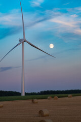 Wind turbine behind straw bale field with full moon