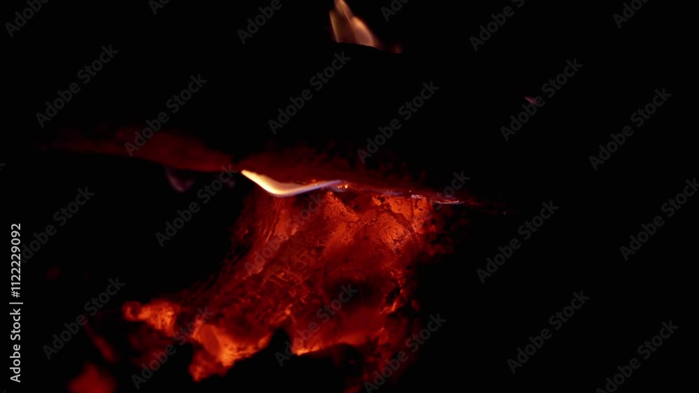 Aufkleber close-up of smoldering embers glowing red in the dark with a burning log above, creating a warm and 
