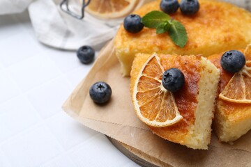 Pieces of delicious semolina cake with blueberries and orange slices on white tiled table, closeup