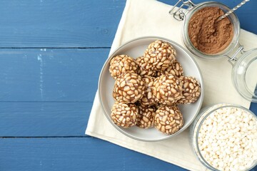 Tasty chocolate puffed rice balls and ingredients on blue wooden table, flat lay. Space for text