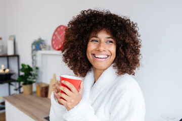 Portrait of happy young beautiful woman in bathrobe enjoying hot coffee in the morning standing in...
