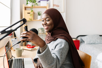 Happy young gen z african woman working on laptop recording podcast at home. Young black content...