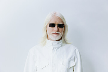 stylish man with long white hair and glasses, wearing a white outfit, standing against a...