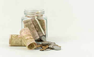 Pkr 10 Pakistani Rupees Currency Bank Notes and multiple coins with a glass jar on a white...
