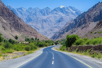 Naklejka premium Asphalt road winds through a valley, majestic mountains in the background. Ideal for travel, adventure, and nature-themed projects.