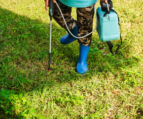 Gardeners in full-coverage clothing spraying herbicides in an outdoor lawn. Spraying to kill weeds....