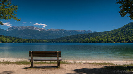 Obraz premium Relaxing bench by a serene lake surrounded by mountains on a sunny day