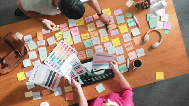 Top view of smart designer holding color palette while project manager looking at design and choosing color for program. Professional businesswoman taking a note while design creative logo. Symposium.