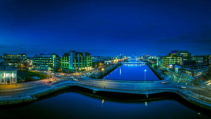 A dusk view of Dublin's modern skyline with the iconic green-lit Bank of Ireland building, a river...
