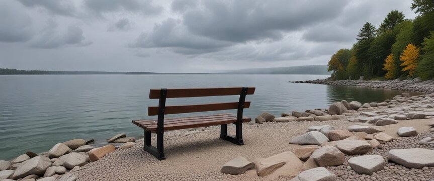 A quiet wooden bench sits atop the rocky shoreline of Pewaukee Lake gazing out onto the serene waters on a cloudy gray day, shadows, peaceful