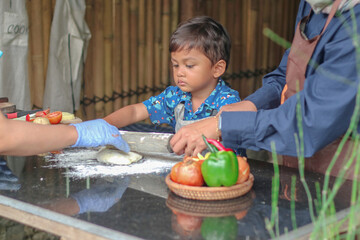 Mother's hands helping her son to roll out a dough, close up