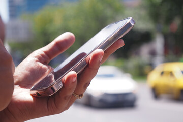 A person holding a smartphone on a busy urban street filled with traffic