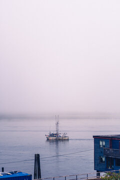 A foggy morning in a Pacific Ocean bay with a boat coming out of the gloom and a pier deck on the foreground