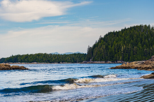 A sunny morning on a beach in the Pacific Ocean with mountains and vegetation in the background and cloudy blue skies and beautiful waters