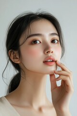 A young Asian woman touches her face with healthy skin and perfect clean facial features isolated on a white background. 