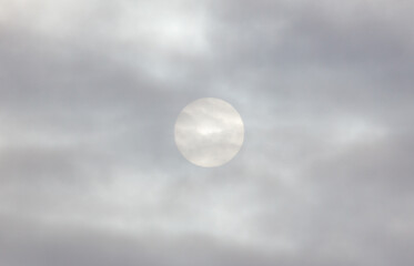 A cloudy sky with a white sun in the middle