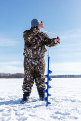 Naklejka premium A man in camouflage clothing is standing in the snow with a blue ice auger