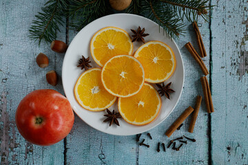 A white plate of vibrant orange slices surrounded by star anise and cinnamon sticks, cloves,...
