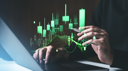Financial analysis with green candlestick chart on screen, person working with laptop and stylus.