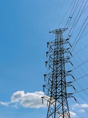 A tall electrical transmission tower standing against a clear blue sky with a few scattered clouds. The structure supports multiple power lines, indicating its role in energy distribution.