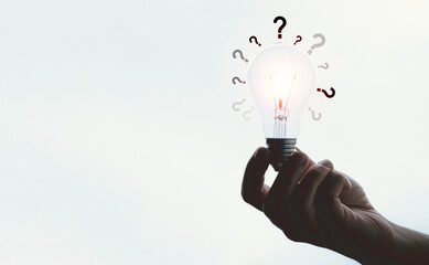 Hand holding glowing lightbulb with question mark and copy space for creative thinking and problem...