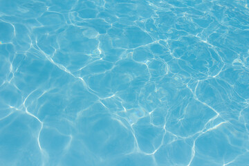 Obraz premium Clear blue swimming pool water surface with sunlight reflections creating abstract patterns and ripples, evoking a refreshing and tranquil summer vibe.