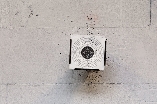 Eine Zielscheibe mit L&ouml;chern von Einsch&uuml;ssen. An der Wand an der sich die Zielscheibe befindet, sind ebenfall Einschussl&ouml;cher von Sch&uuml;ssen, die nicht die Scheibe trafen.