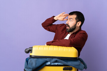 Traveler caucasian man with a suitcase full of clothes over isolated purple background with surprise expression while looking side