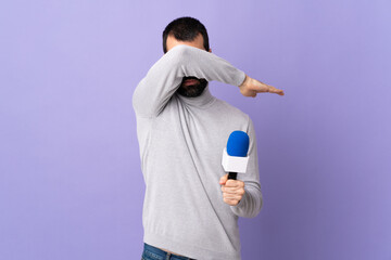 Adult reporter man with beard holding a microphone over isolated purple background covering eyes by...