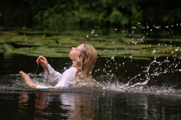 A beautiful blonde young girl is relaxing by the pond.