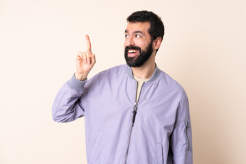 Naklejka premium Caucasian man with beard wearing a jacket over isolated background intending to realizes the solution while lifting a finger up