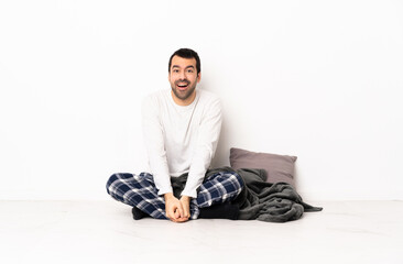 Caucasian man in pajamas sitting on the floor at indoors with surprise facial expression