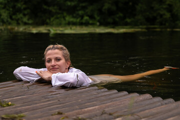 A beautiful blonde young girl is relaxing by the pond.