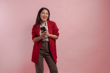 Naklejka premium Excited young Asian woman in a red jacket is holding smartphone with smiling expression.