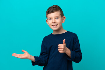 Little kid boy isolated on blue background holding copyspace imaginary on the palm to insert an ad...