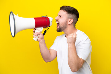 Young caucasian man isolated on yellow background shouting through a megaphone to announce...