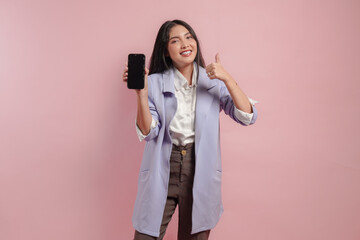 Excited Asian woman gives thumb up hand gesture of approval while showing copy space on her phone.